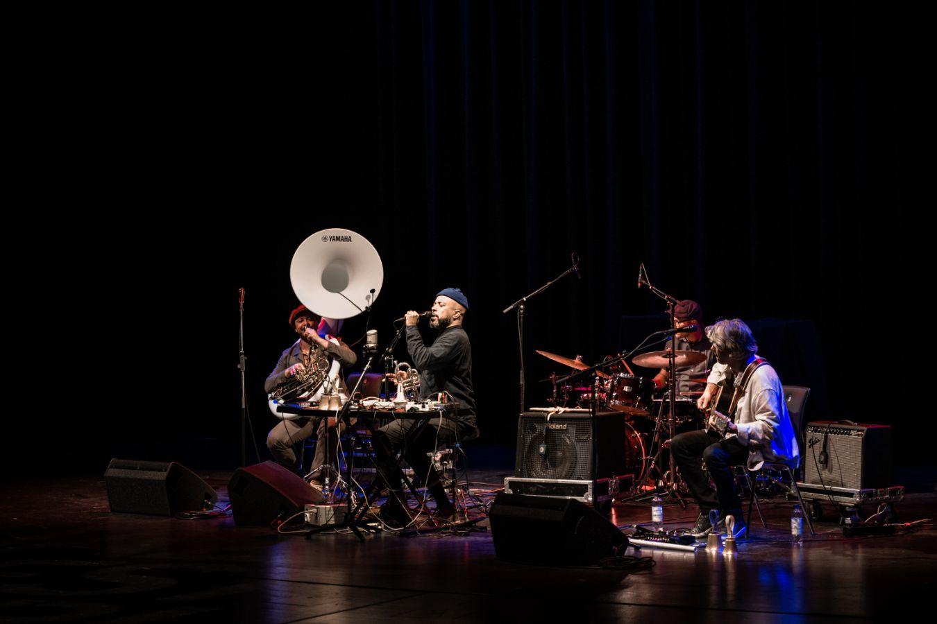 Eine vierköpfige Band mit verschiedenen Instrumenten auf einer Bühne.
