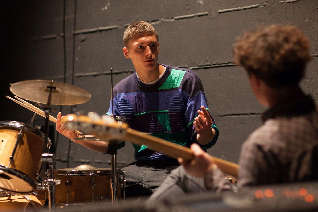 Zwei Jungen machen zusammen Musik. Der spielt Schlagzeug der andere E-Gitarre.