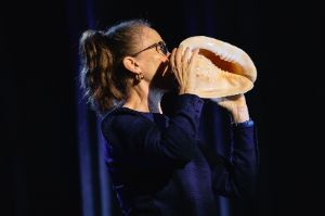 Musician Christine Chapman holds a conch shell to her mouth.