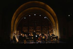 Musiker*innen des International Contemporary Ensemble auf der Bühne. Im Hintergrund ein beleuchteter Bogen, der die Bühne des Theater im Delphi einfasst.