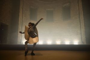 Performerin Miriam Parker tanzt in einem wellenförmigen, skulpturalen Gewand, im Hintergrund die steinerne Wand der St. Elisabeth-Kirche.
