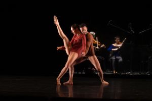 Zwei Tänzer*innen während einer Aufführung, im Hintergrund zwei Streicher*innen.