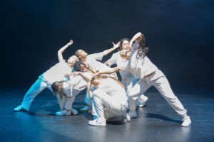 Young dancers in white clothes form a cluster of people in their dance postures.