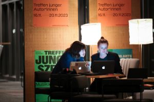 Two young people sit under reading lamps in front of their laptops.