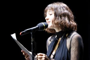 Alexandra Isabel Reis steht in einem dunkelblauen Hosenanzug vor einem Mikrofon und liest von einem Zettel.