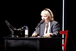 Carolin Schäfer sits on a red chair at a black table and speaks into a microphone.