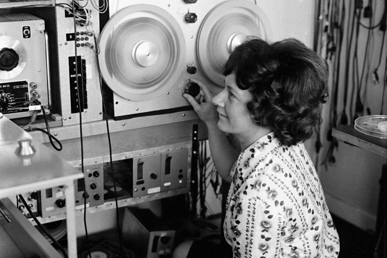 A woman with short hair turns the knob on a tape recorder.