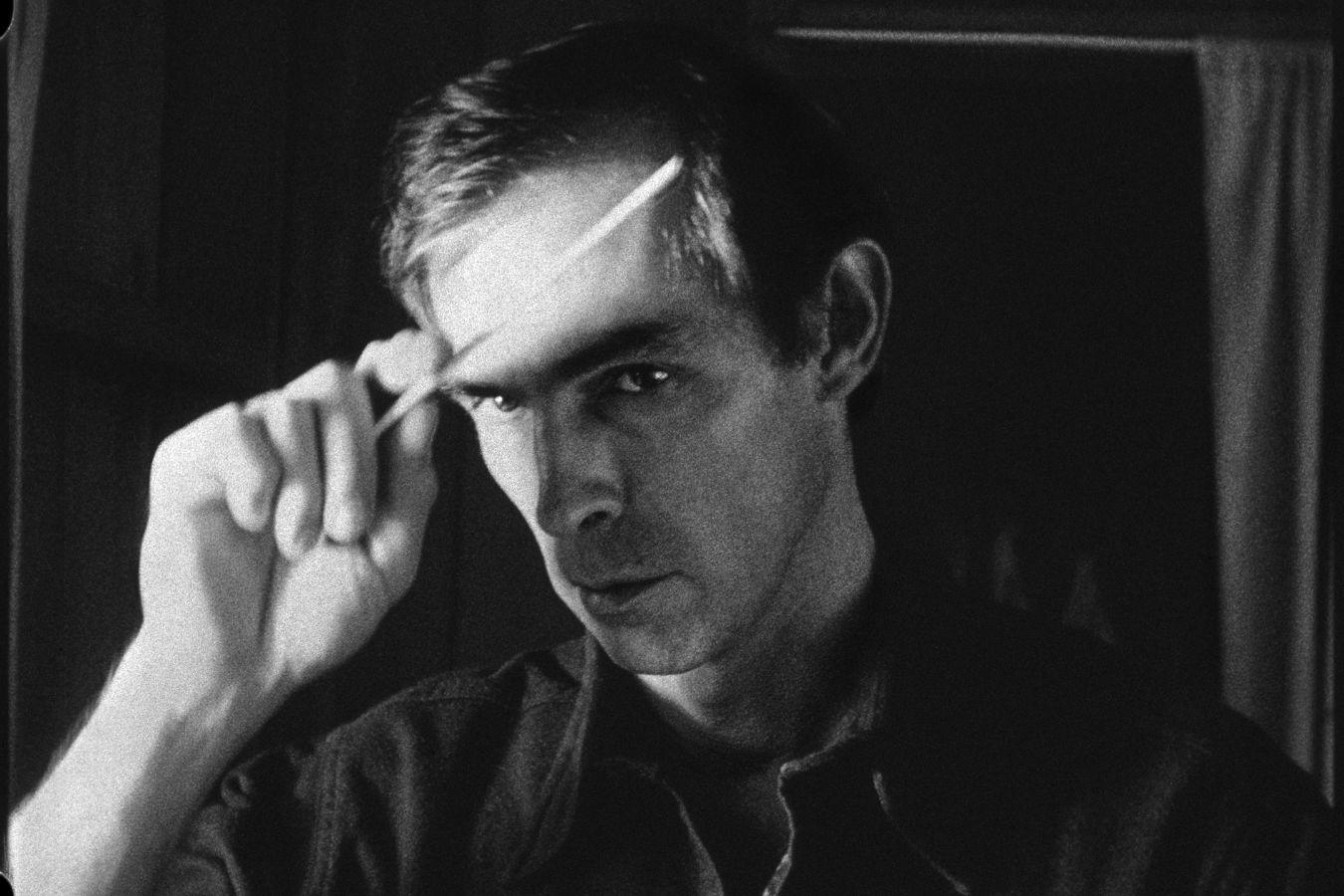 A male person holds a narrow object up to his forehead with one hand and looks intently beneath it.