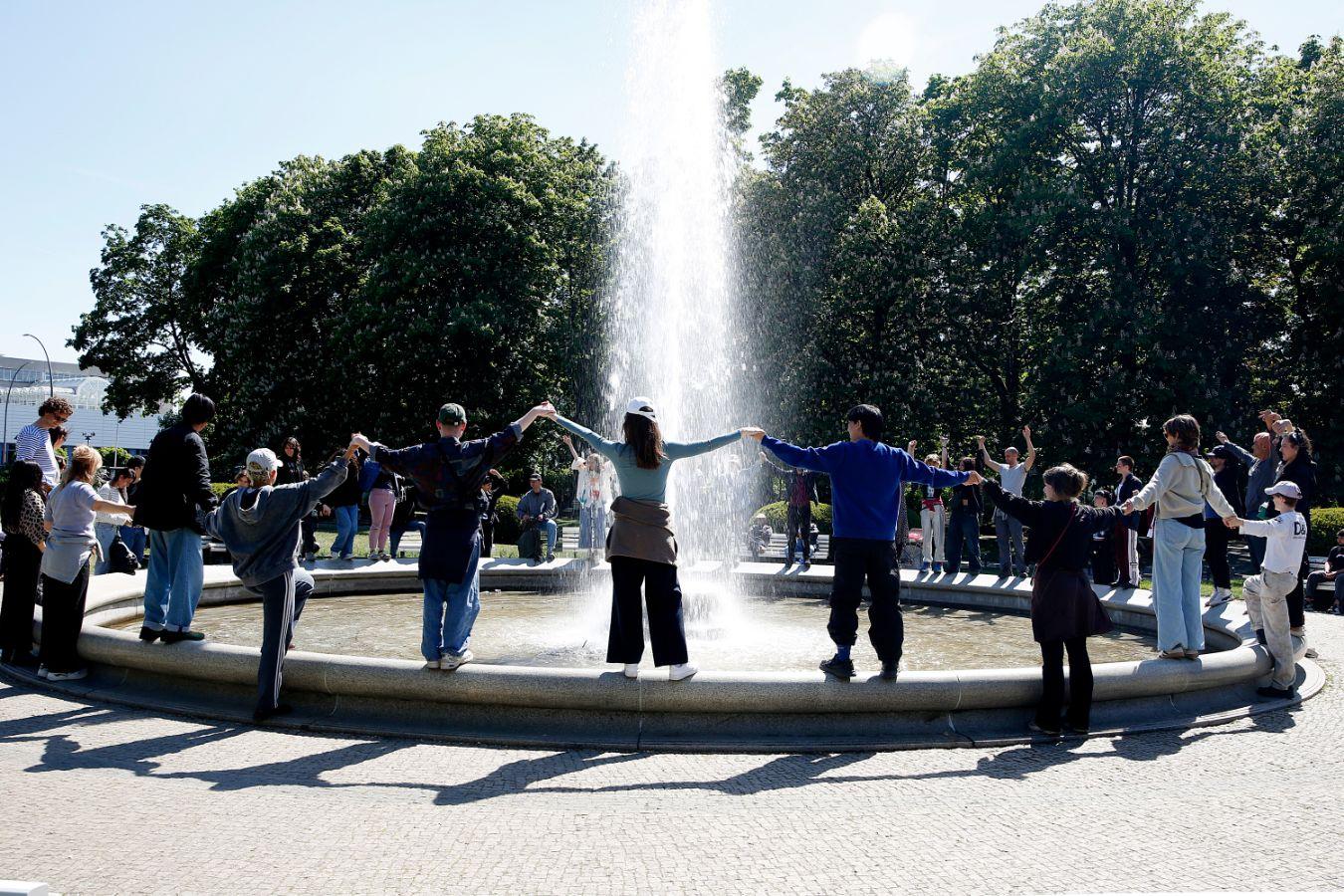A group of people form a circle around a water fountain.