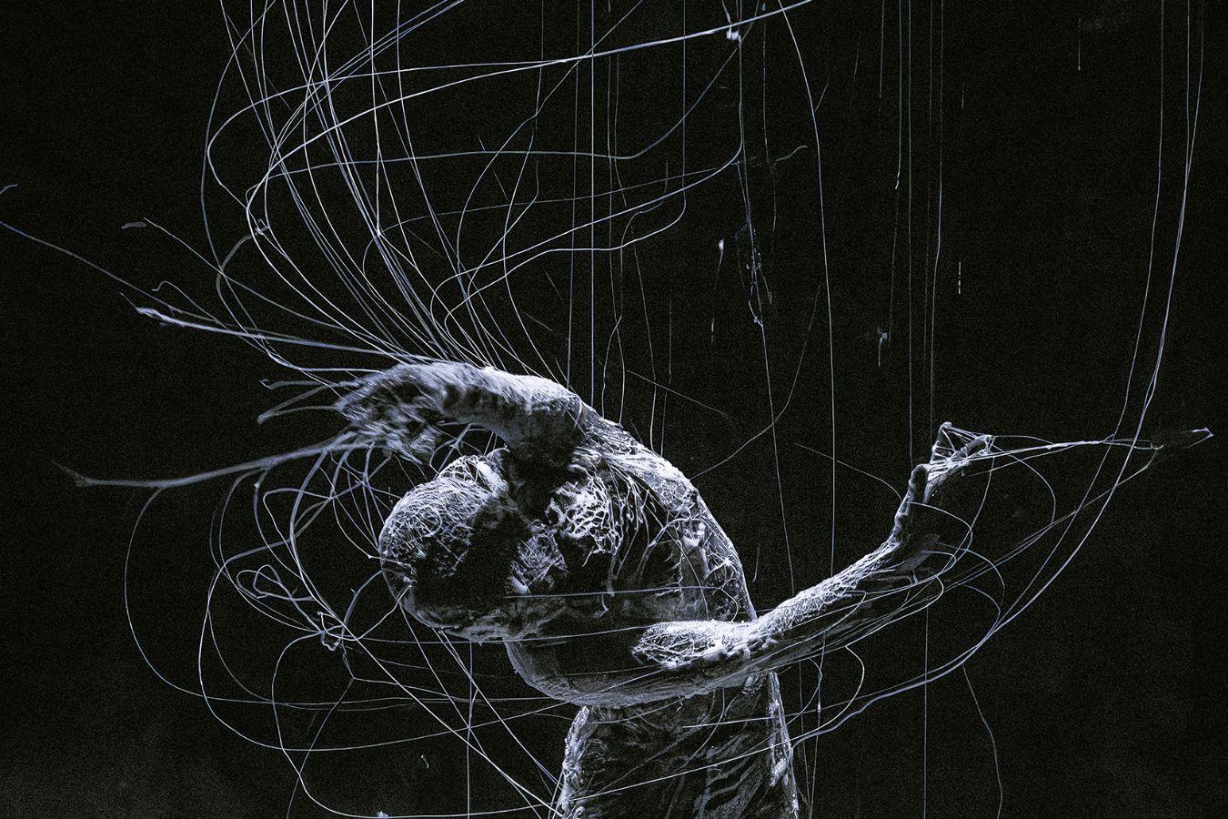 A person surrounded by a white liquid, moving in such a way that threads of the substance stretch from their entire body.