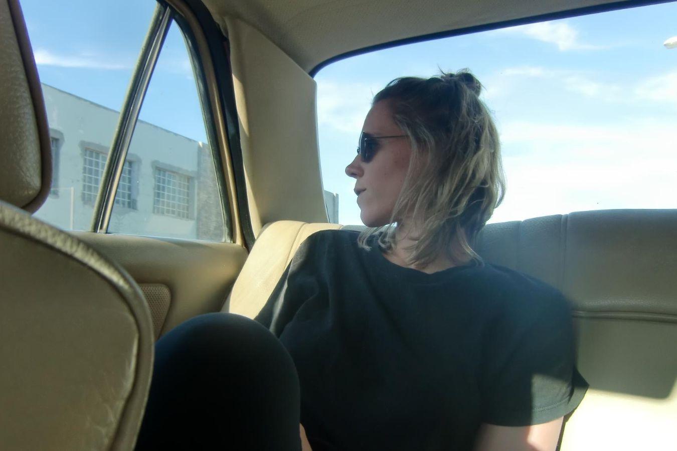 Photo of a person wearing sunglasses sitting in the back seat of a car.