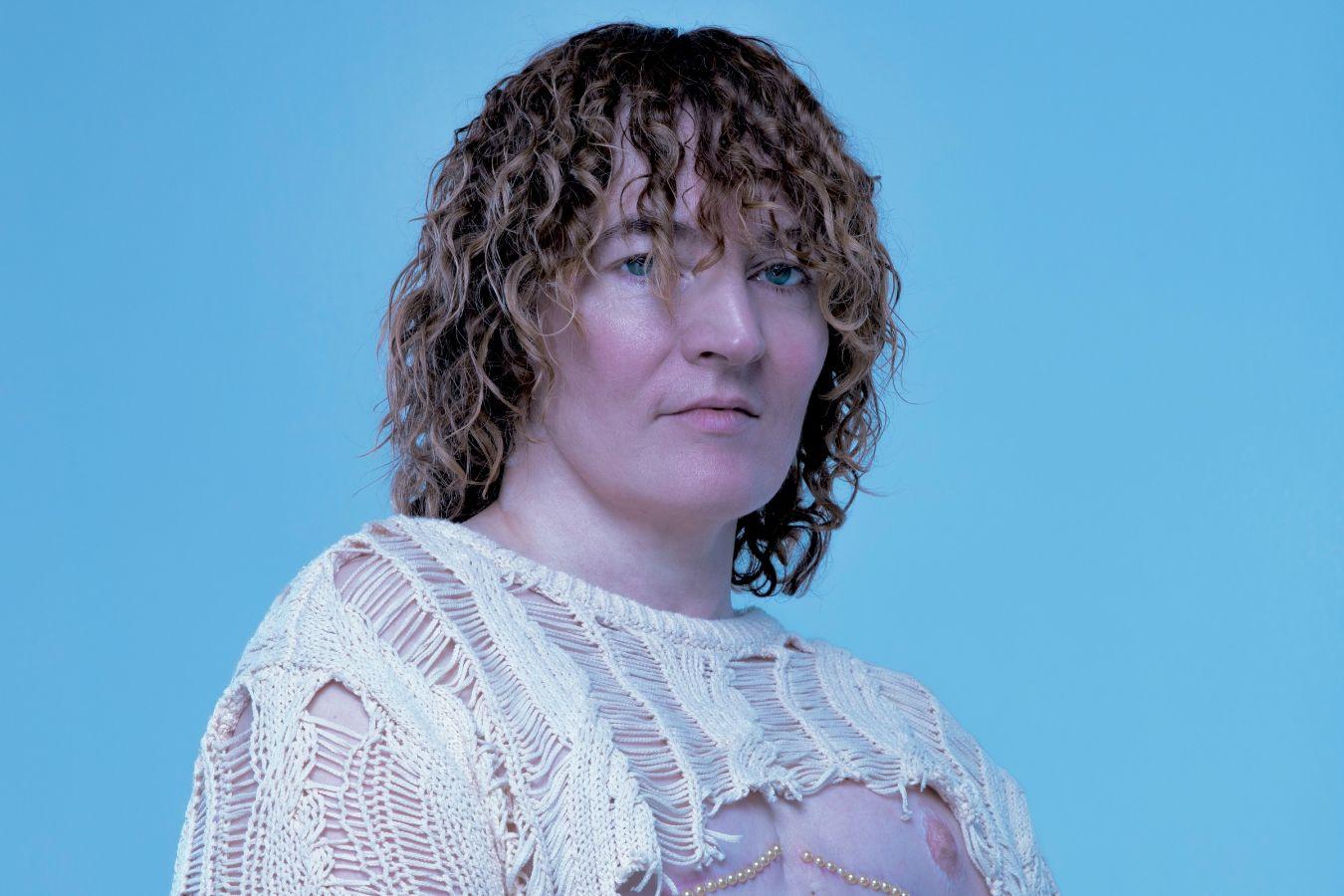 Portrait of a person with curls and a cropped knitted top.