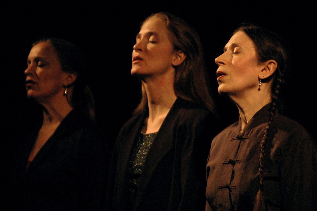 Three people sing with their eyes closed. The lighting is gloomy.