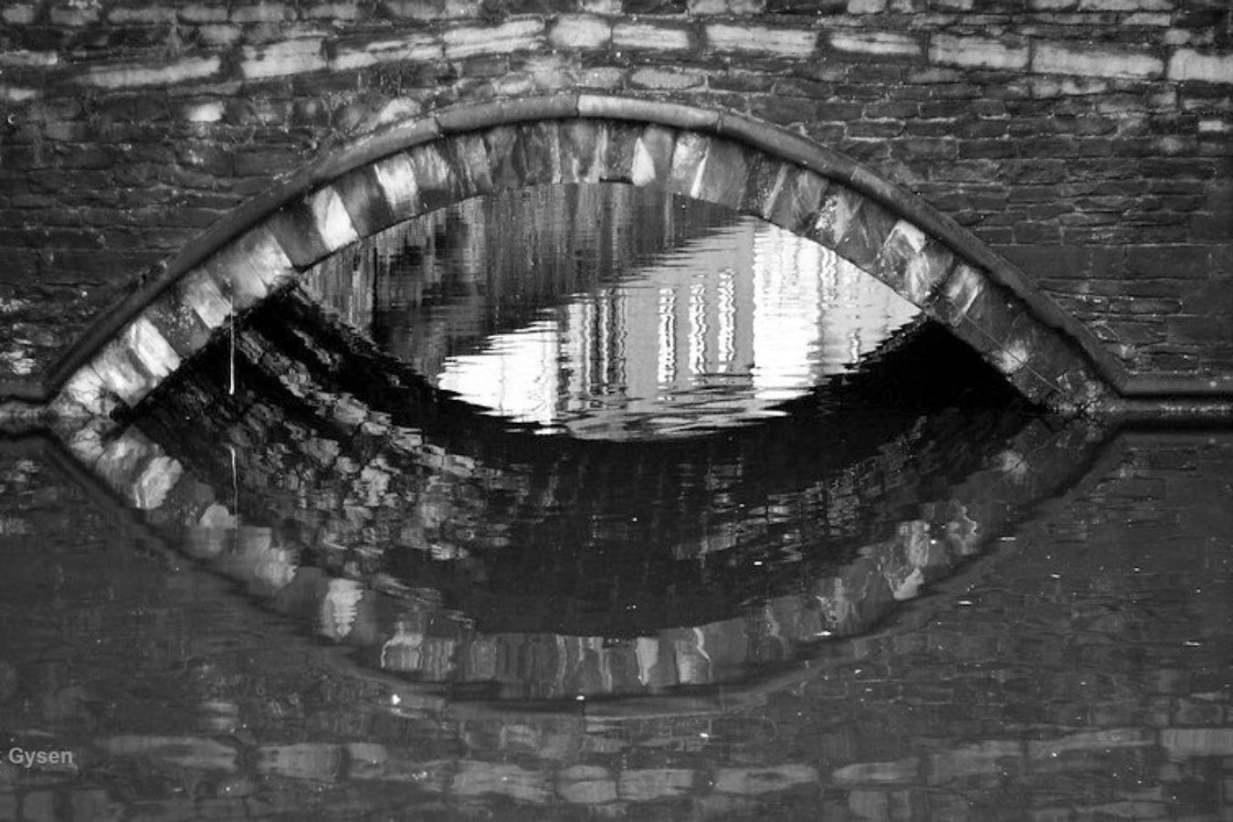 The arch of an old stone bridge is reflected in the water and looks like an eye.