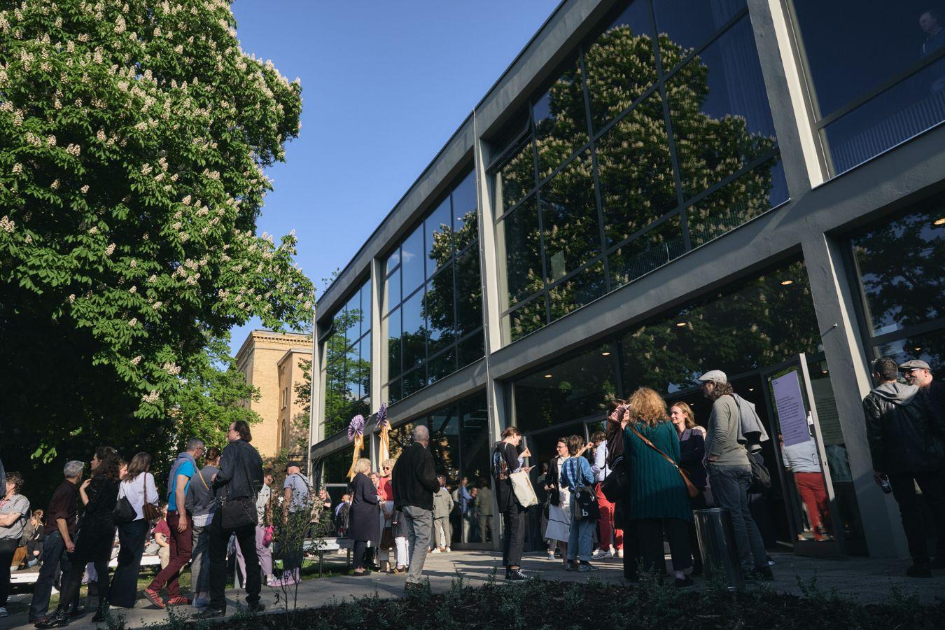 Front entrance of the Berliner Festspiele. It is sunny and people are standing and chatting in front of the building.