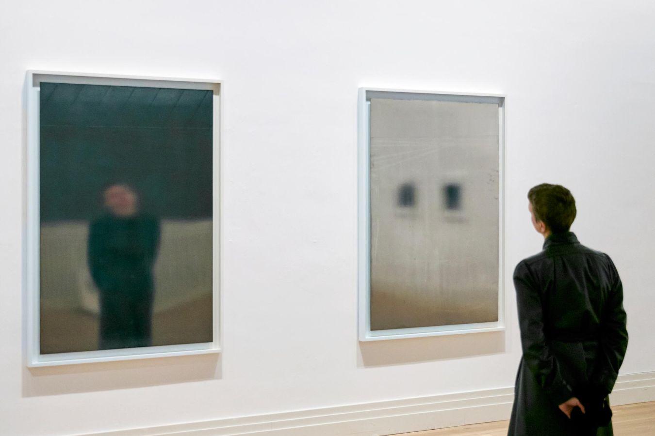 Eine Person, die mit dem Rücken zur Kamera vor zwei rechteckigen, spiegelartigen Kunstwerken steht.