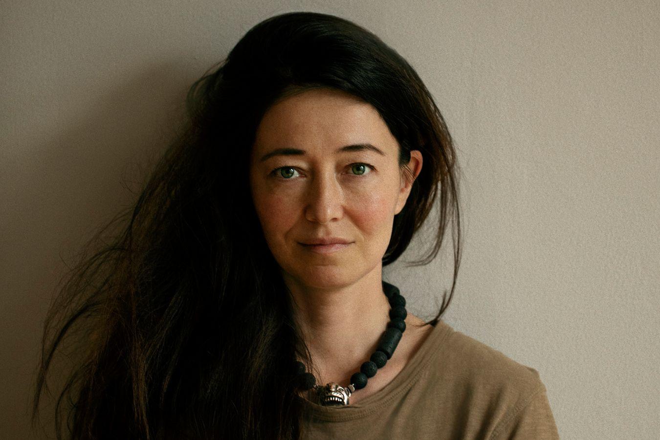 Porträt von einer Person mit langen dunklen Haaren vor einer grauen Wand.