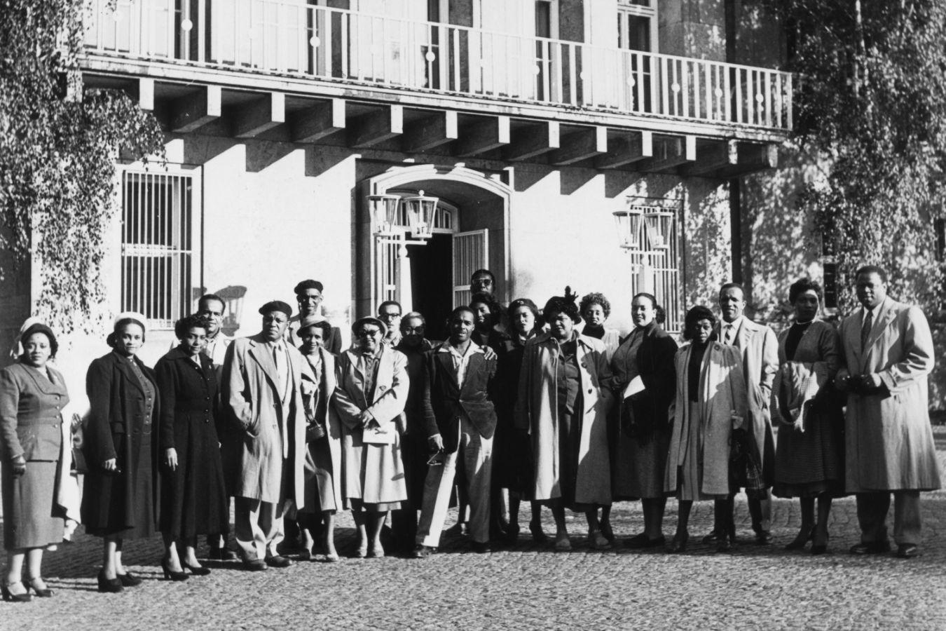Black-and-white group portrait of the ensemble in front of a building
