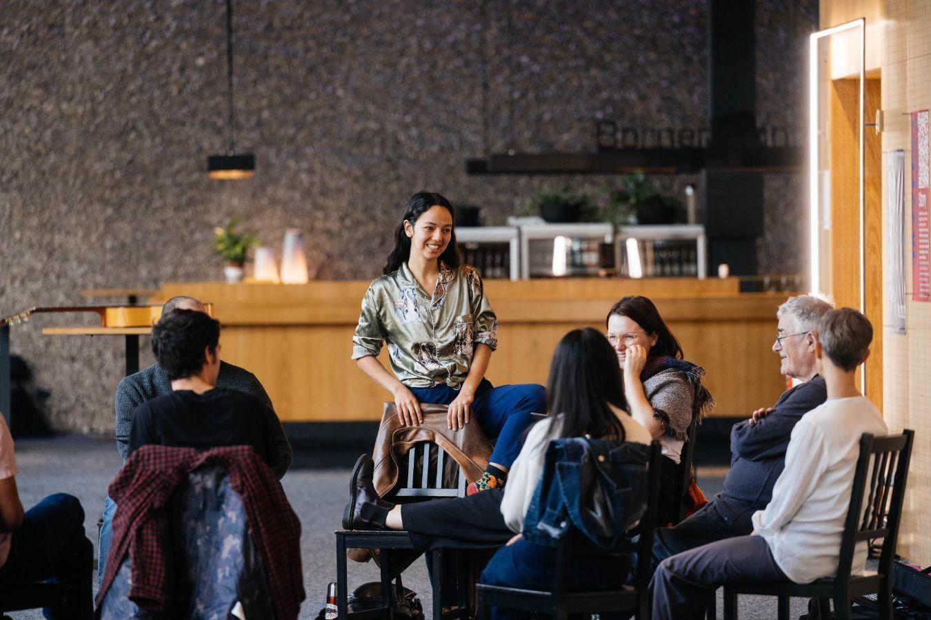 Einige Menschen sitzen im Kreis und eine steht.