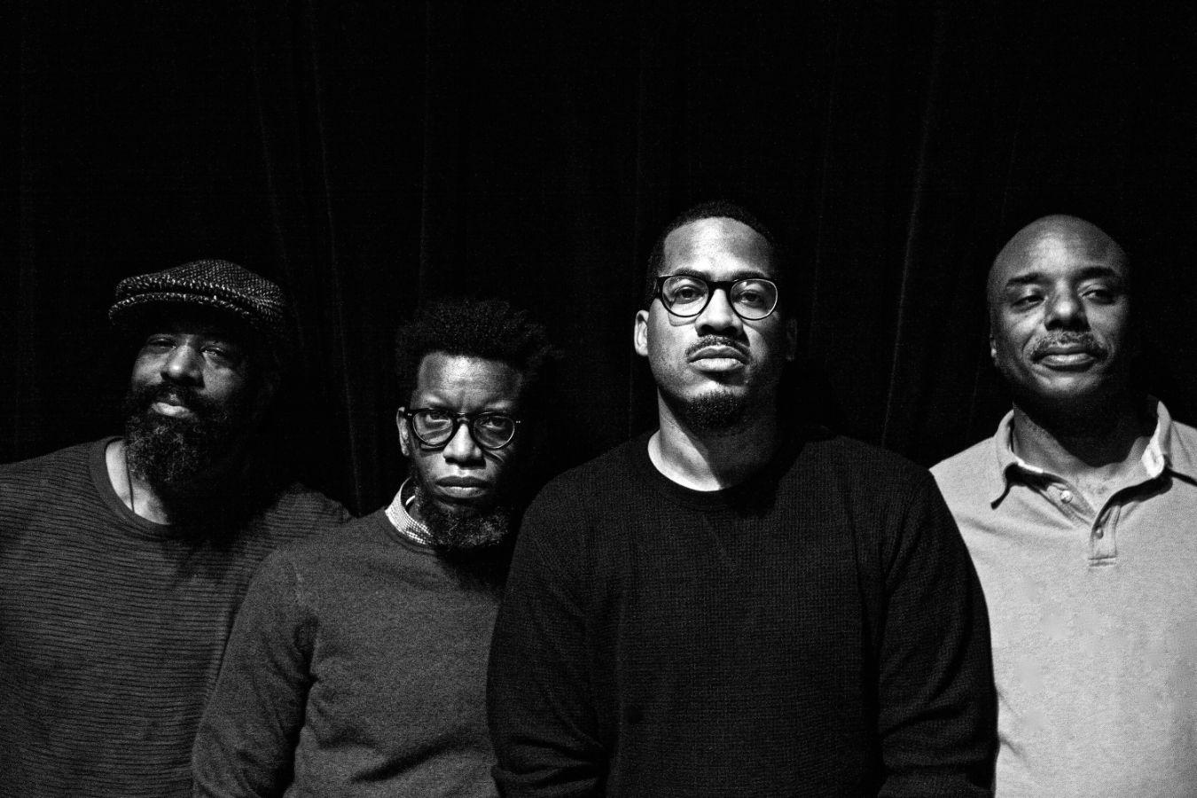 Vier Musiker stehen nebeneinander und schauen ernst