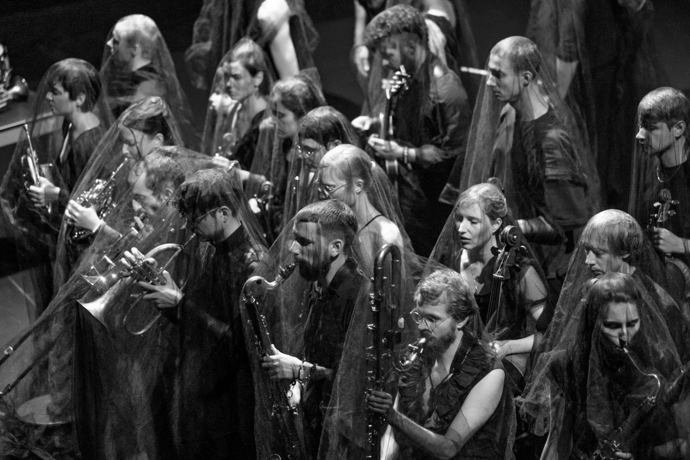 Musiker*innen spielen ihre Instrumente. Durchsichtige Tücher liegen über ihren Köpfen.