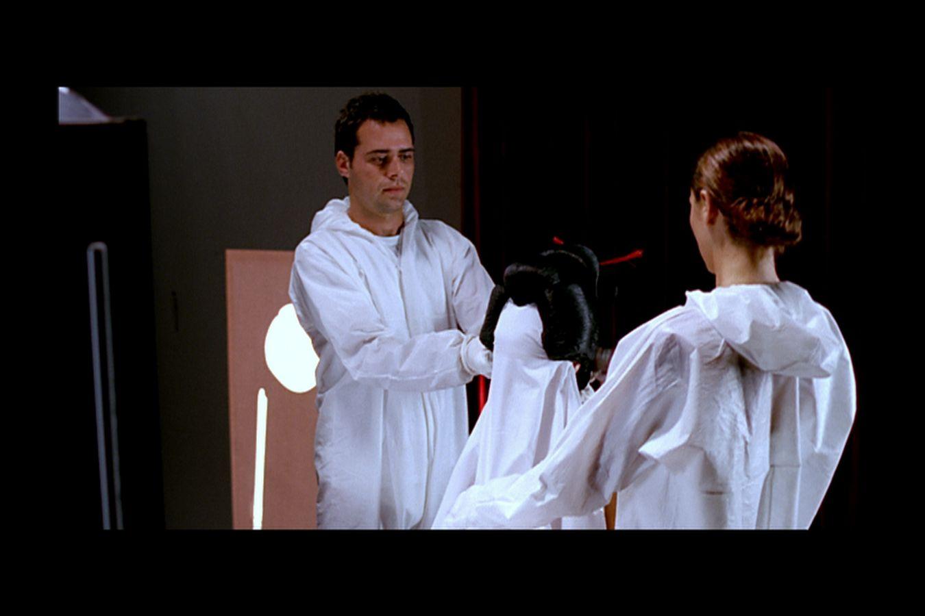 Two persons in a dark room, both of them wearing a white full body-suit