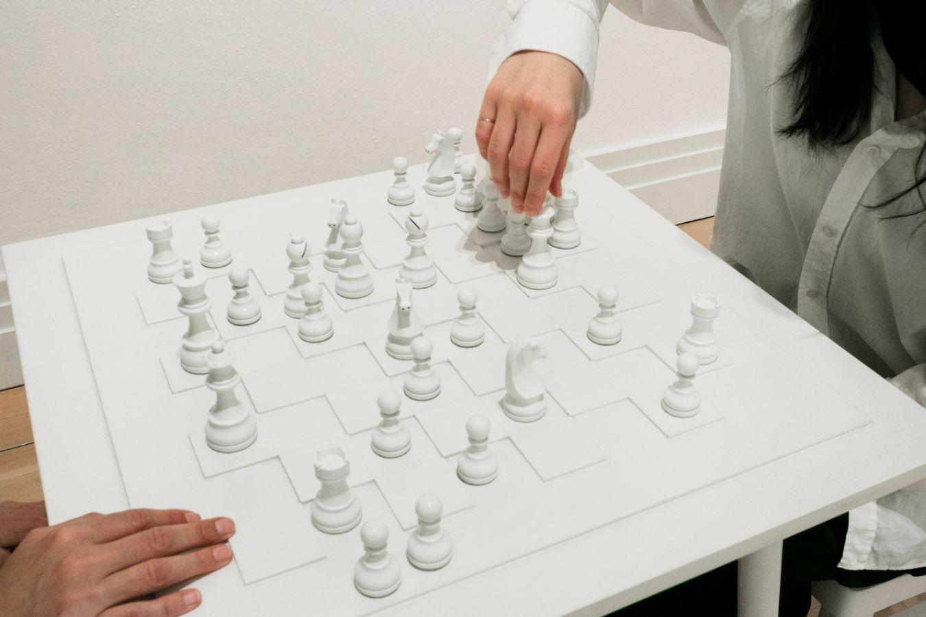 Two people are playing chess with only white chess pieces. Only their hands can be seen.