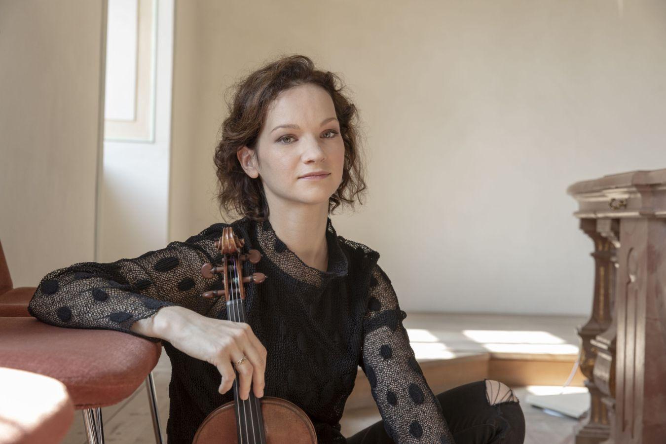 A young woman is sitting on the floor with a violin in her right hand.
