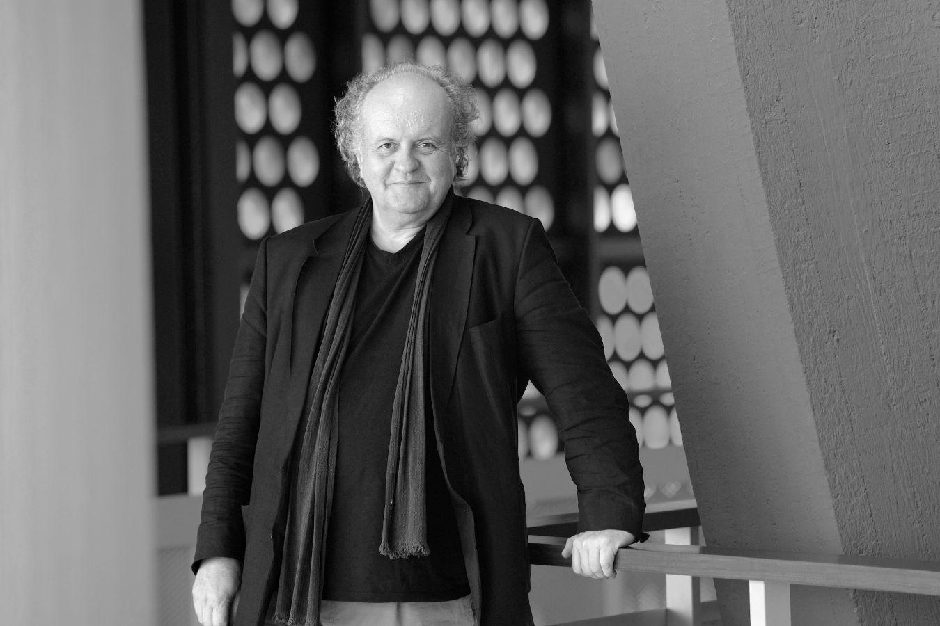 An older man wearing a jacket and scarf leans on a railing in the foyer of the Philharmonie Berlin.