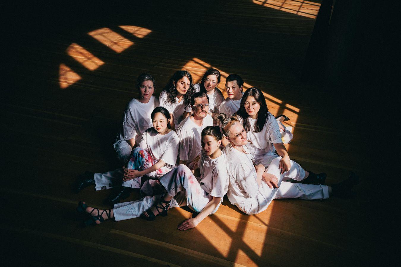 A group of people are sitting on the floor. They are illuminated by light shining through a box window.