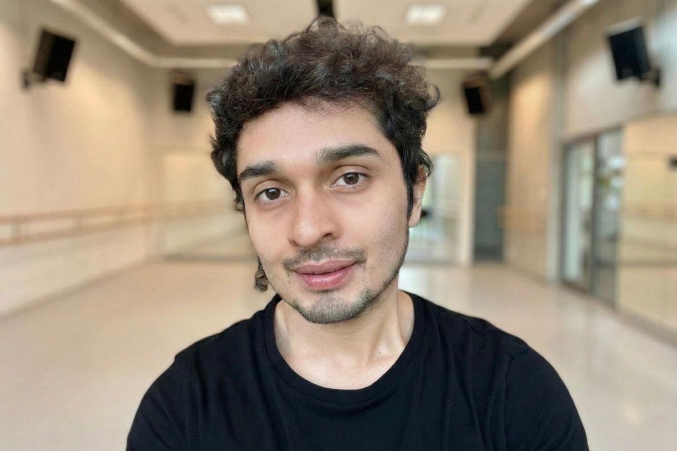 A man with short brown hair and a beard wearing a black top in a dance studio