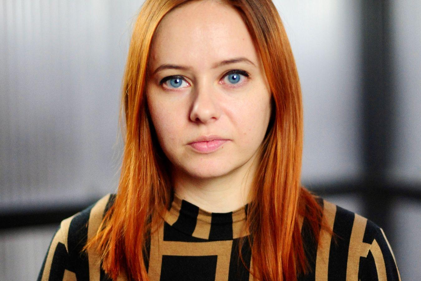 A person with medium-length red hair wearing a jumper with a graphic pattern