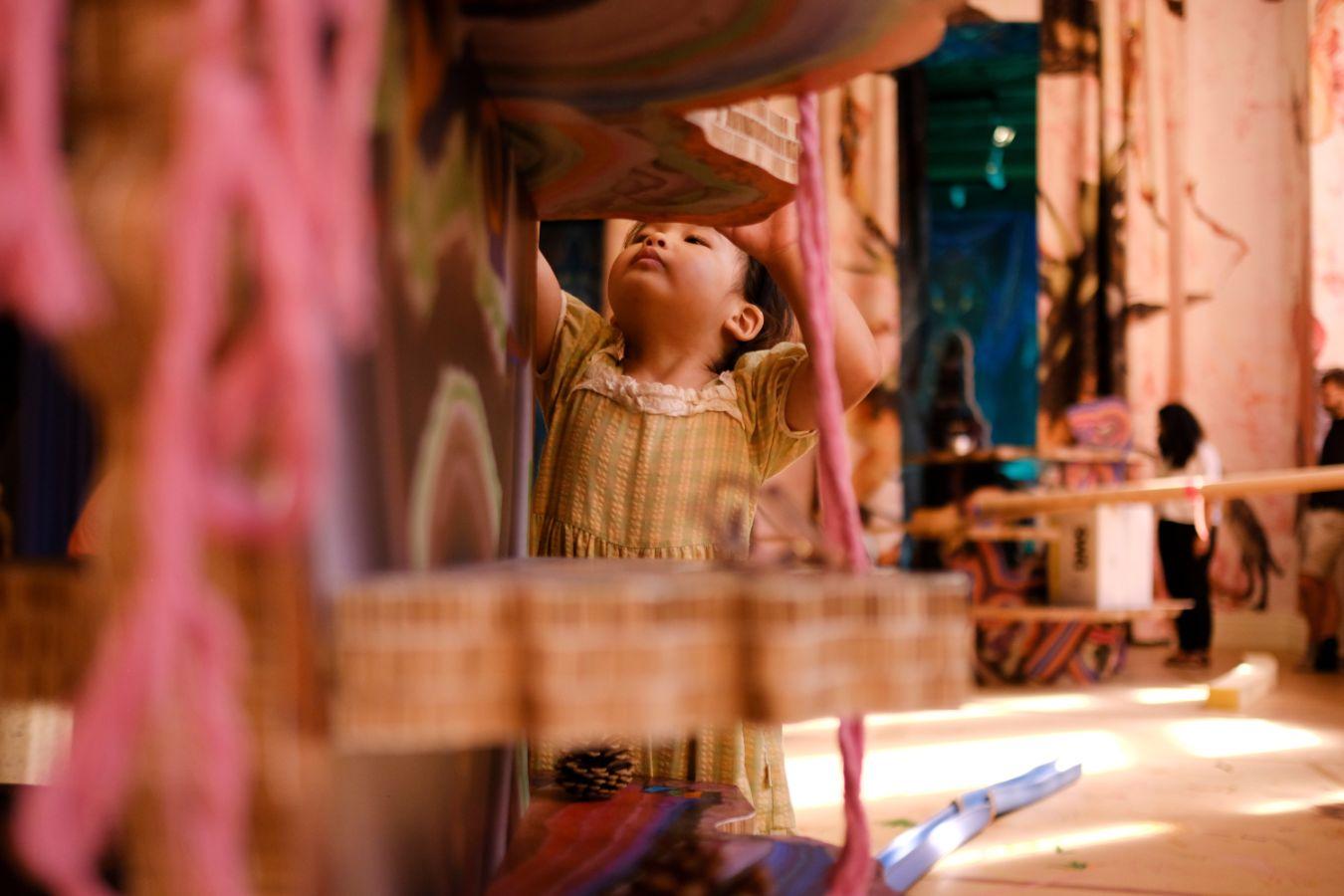 Ein Kind kniet hinter einem Kletterelement; im Raum hängen bunte Vorhänge mit Dinosauriern.