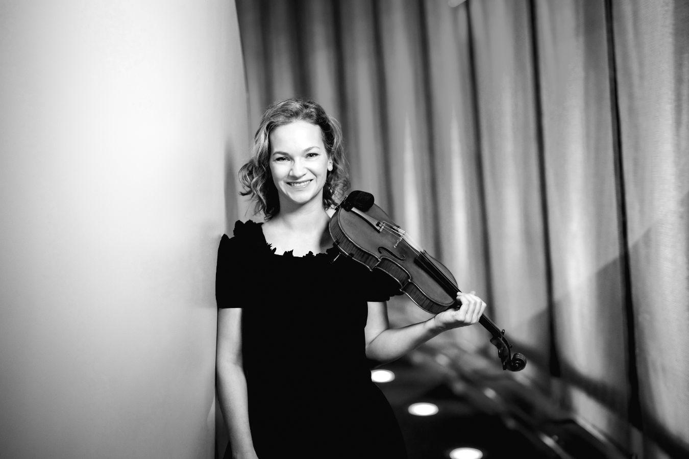 A violinist is leaning against the wall and looking at the camera.