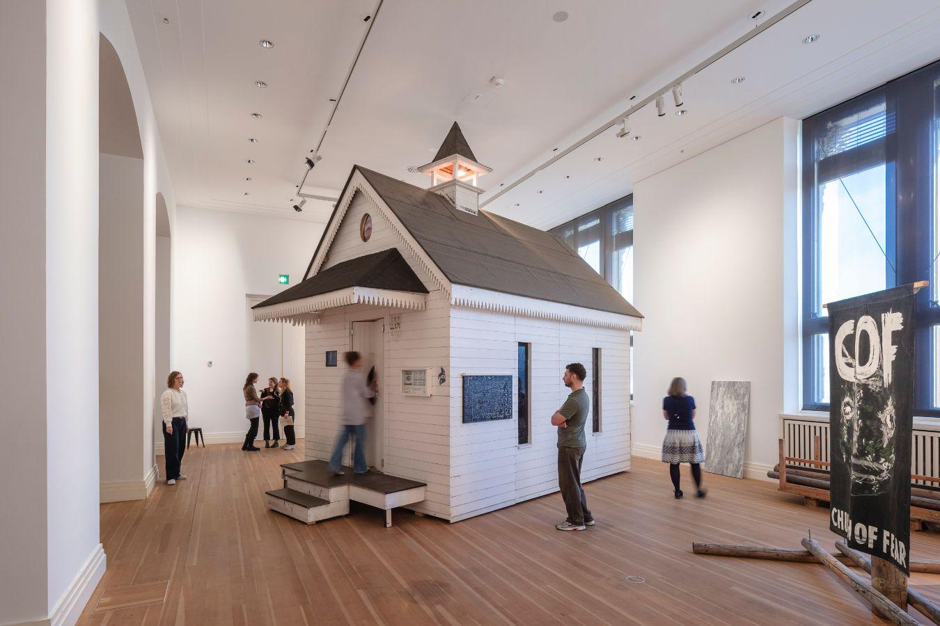 Ausstellung mit Modell eines weißen Gebäudes, Personen stehen um das Gebäude.