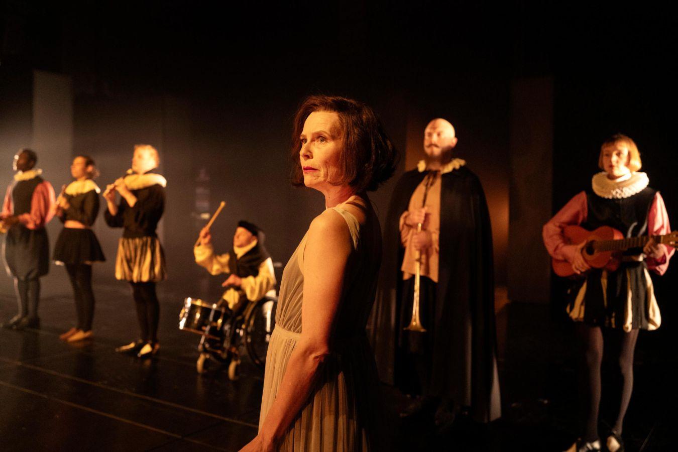 An ensemble in historical costumes reminiscent of the Shakespearean era performs music onstage.