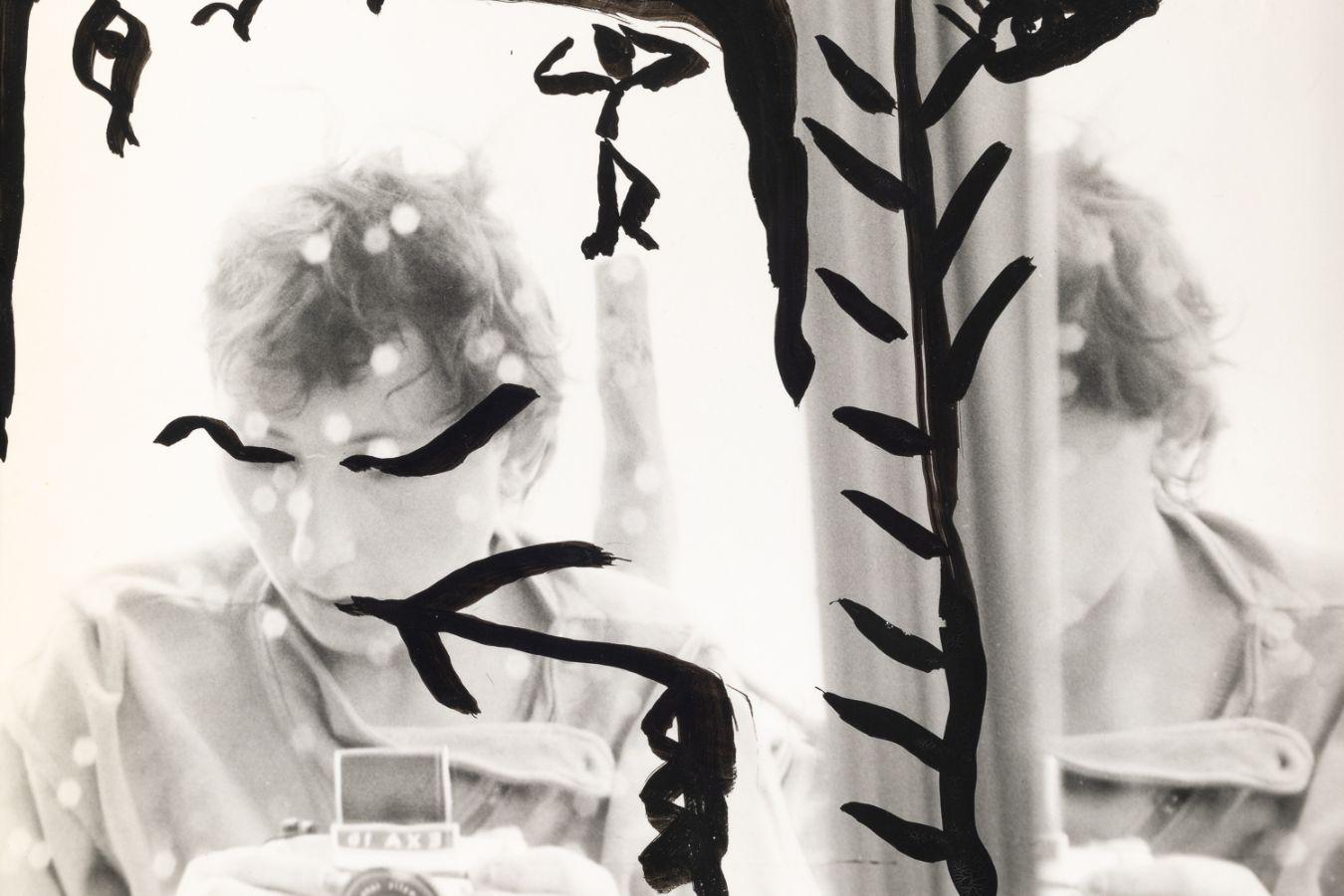 A self-portrait by Gabriele Stötzer, painted with black patterns, capturing herself in the mirror with an analog camera.