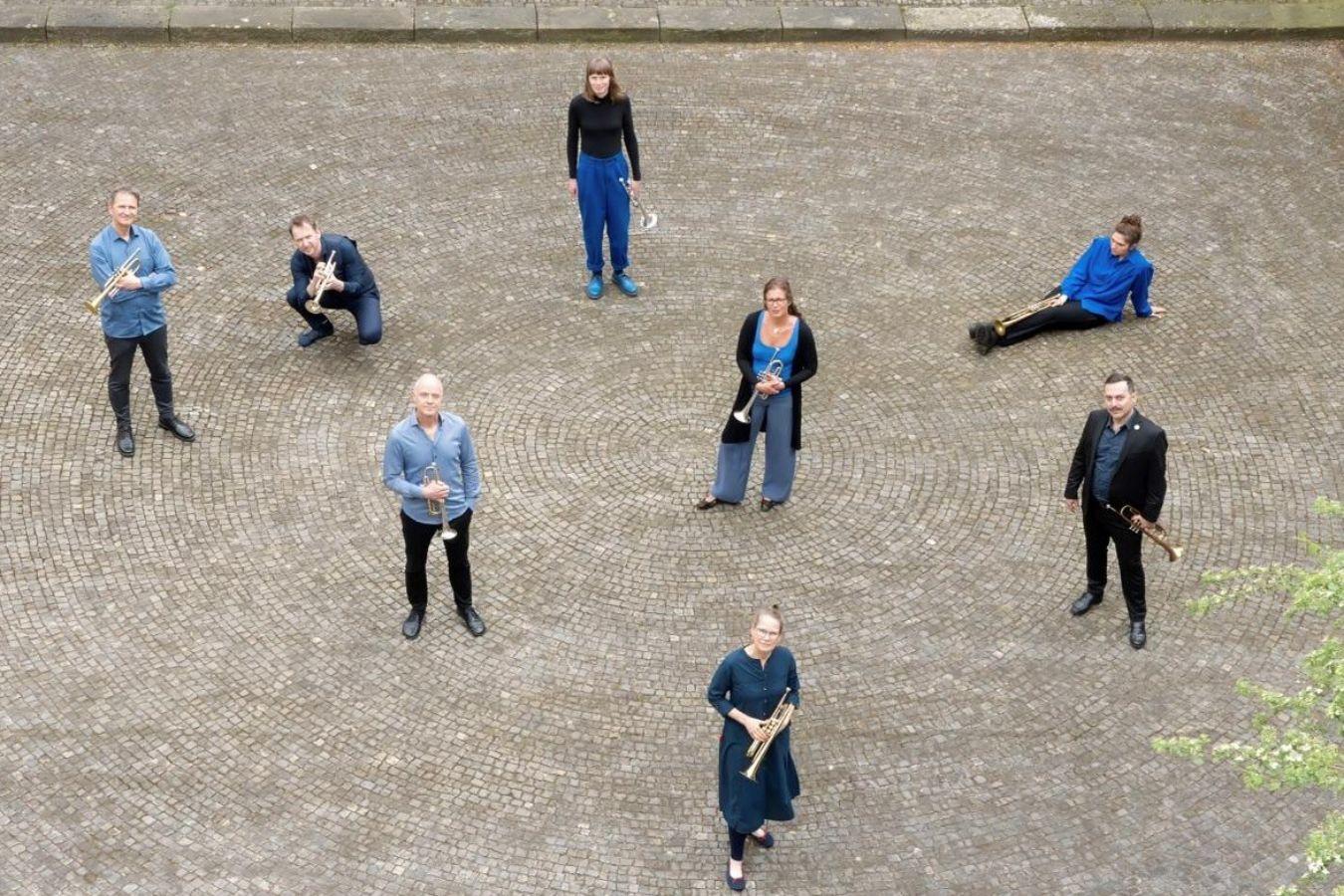 Aufnahme des Trompetenensembles The Monochrome Project aus der Vogelperspektive. Die Musiker*innen befinden sich auf einem Platz und halten ihr Instrument in den Händen.