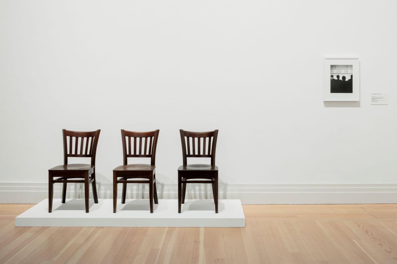 Three wooden chairs stand next to each other on a white pedestal.