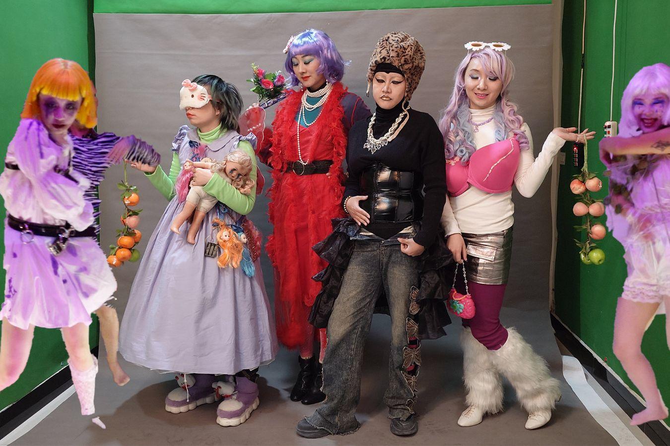 Six people in colourful costumes stand in front of a silver photo background.