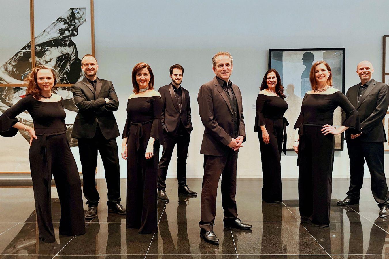 Eight people dressed in black stand in a room with pictures on the walls.