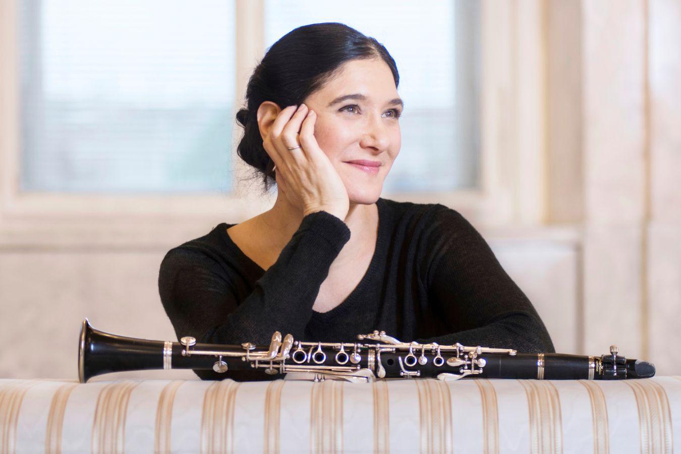 Porträt: Kam stützt das Gesicht in eine Hand und lächelt. Vor ihr liegt eine Klarinette.