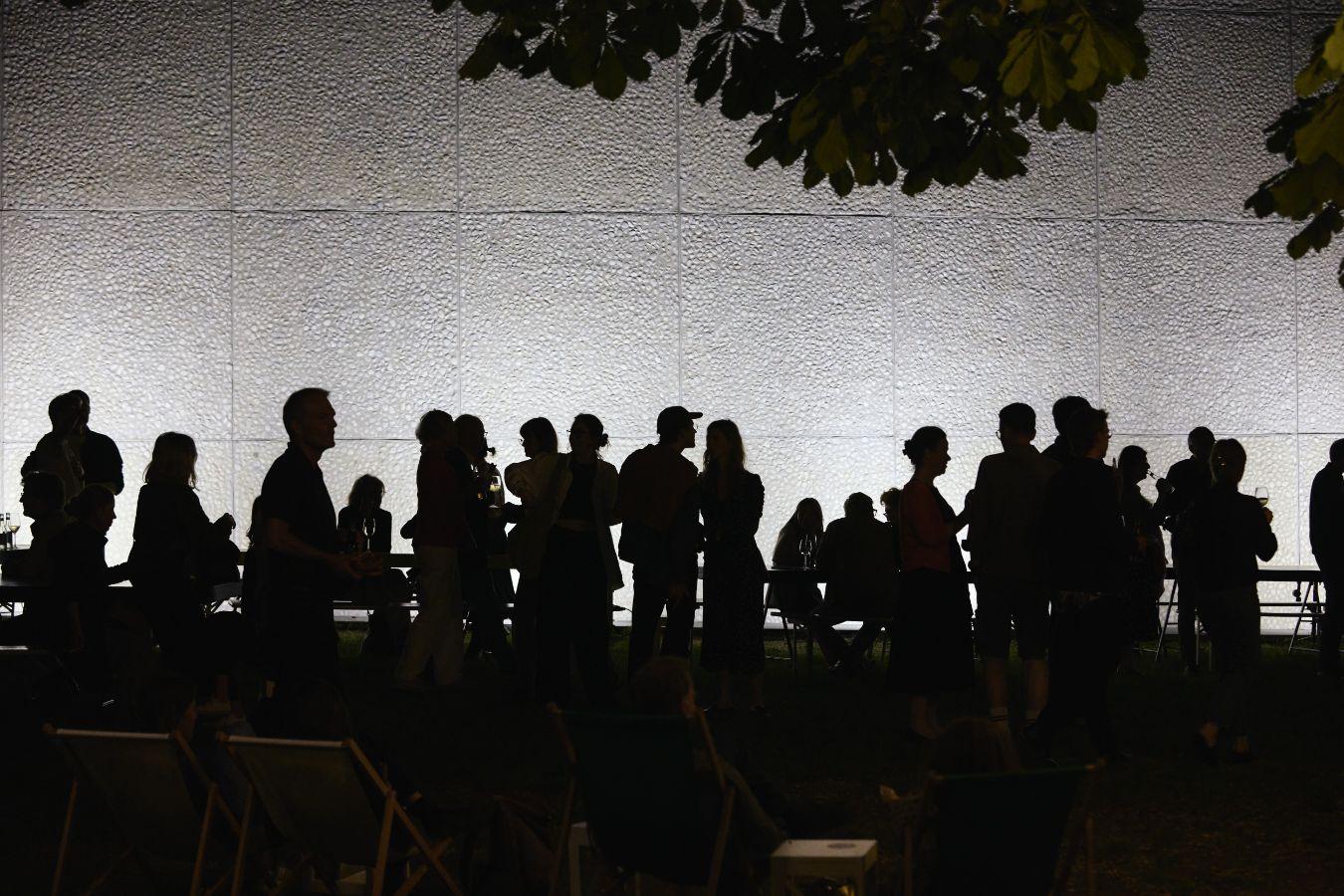 Eine Gruppe von Menschen steht bei Nacht im Garten des Haus der Berliner Festspiele.