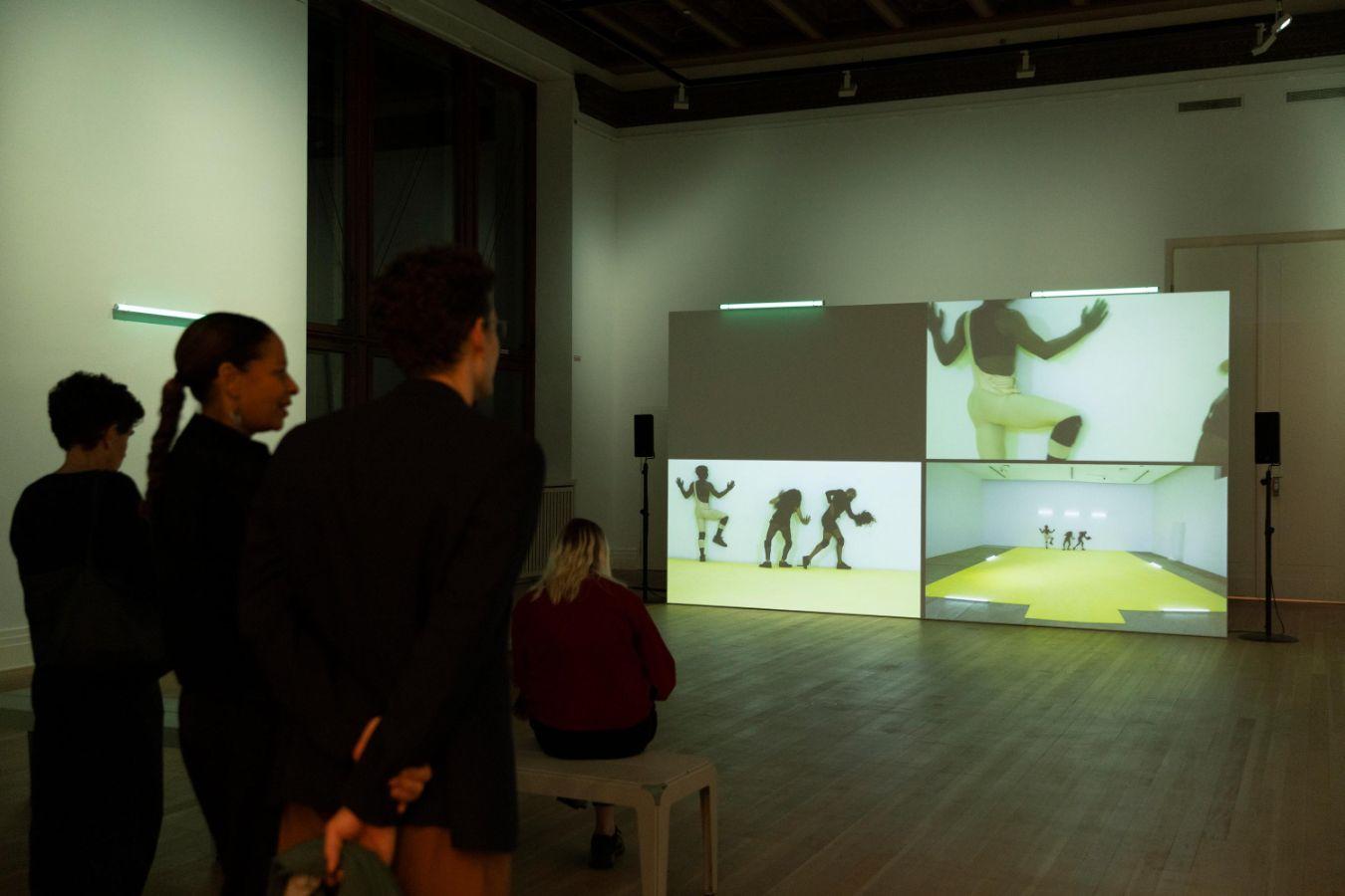 A group of people is looking at a screen in front of them displaying three different scenes from a performance.