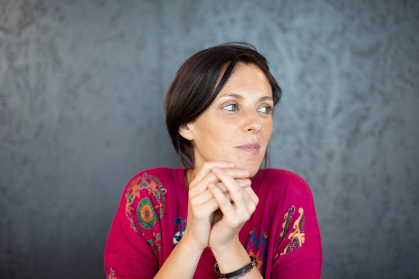 A woman with brown hair leans her head on her hands and looks to the left.