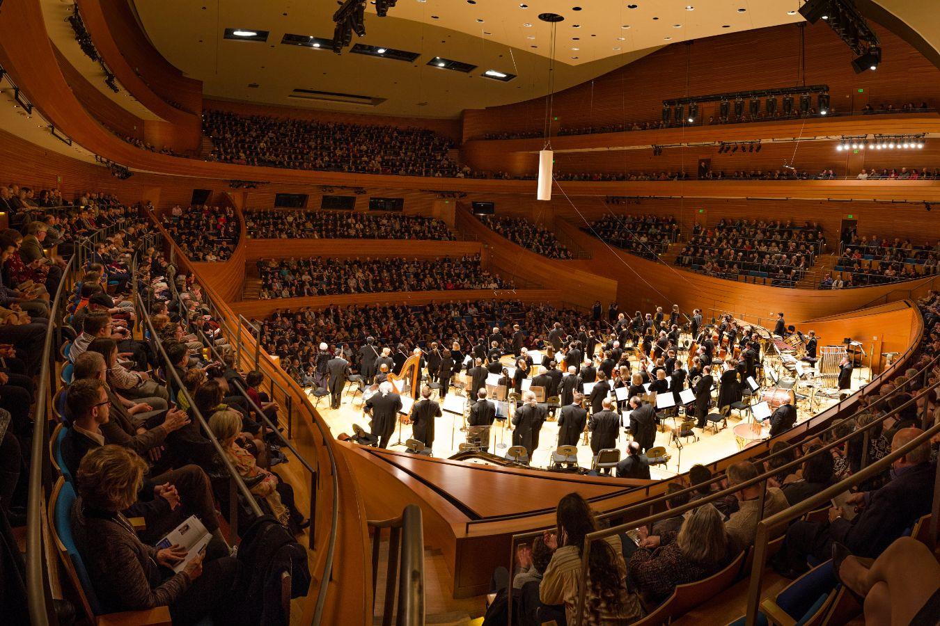 The inside of a concert hall with lots of people and an orchestra in the centre