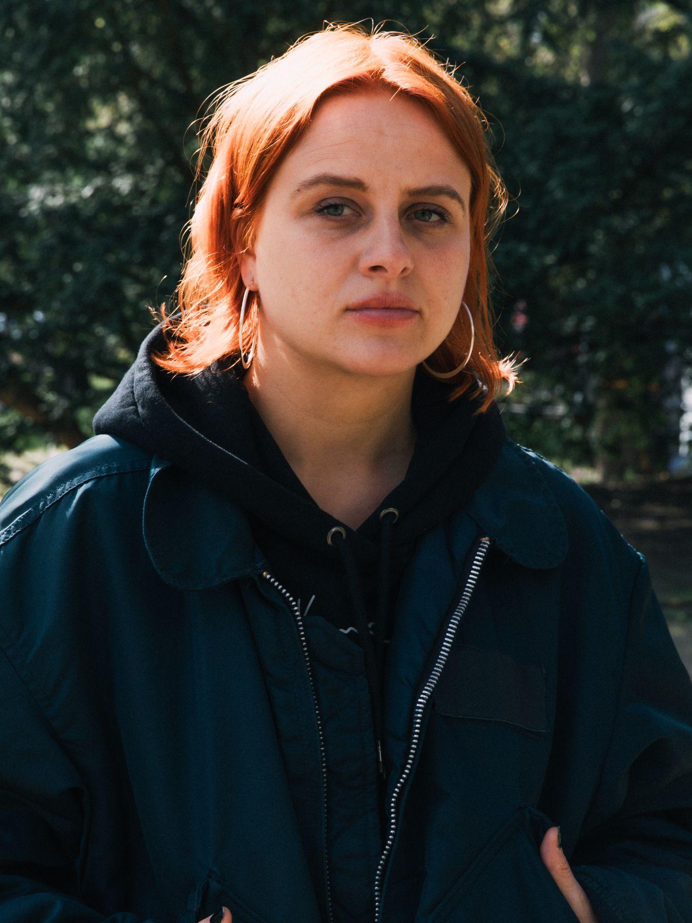 Eine Frau mit roten mittelangen Haaren in einem schwarzen Oberteil draußen