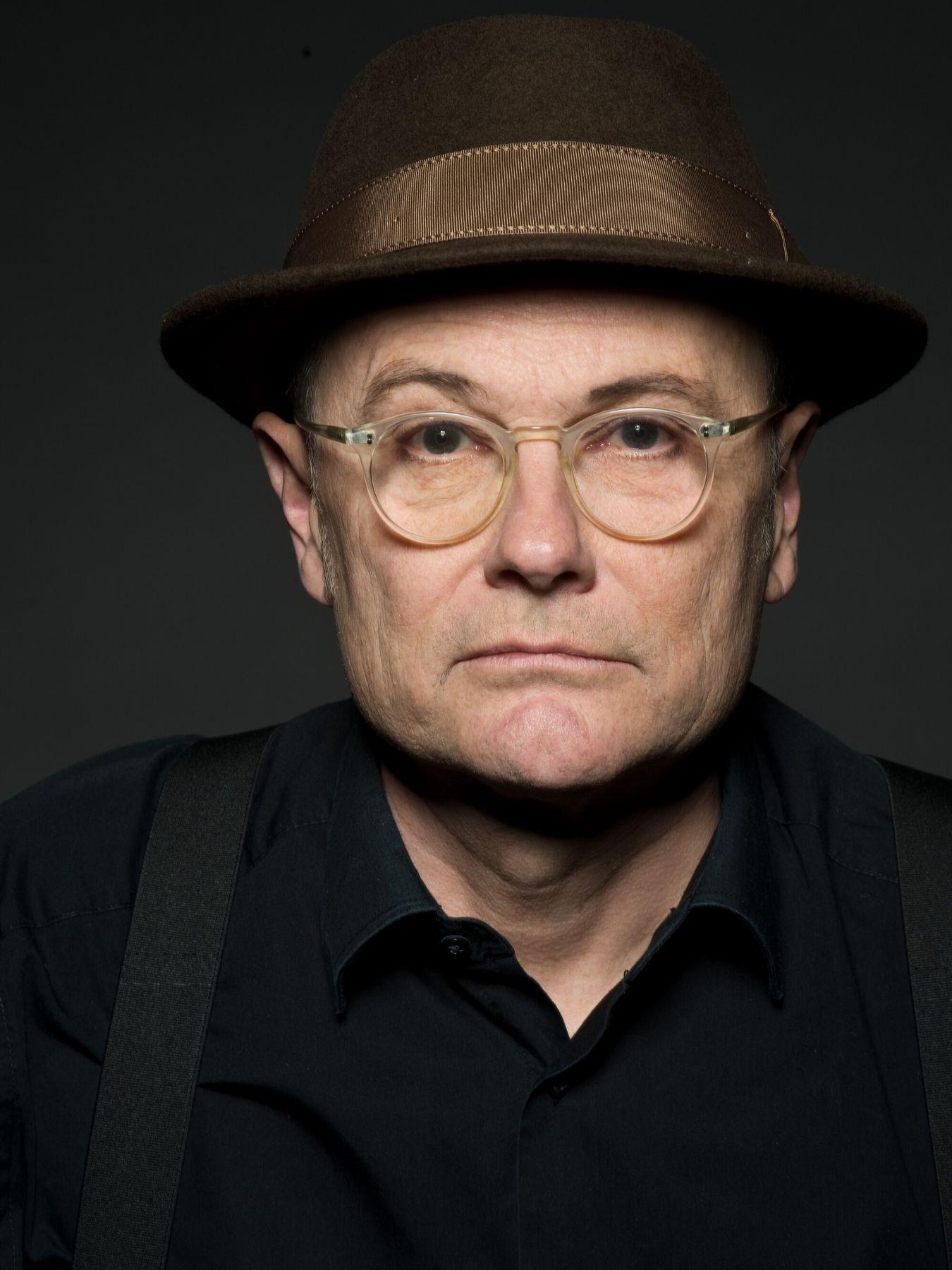 A man with glasses and a hat looks seriously into the camera.