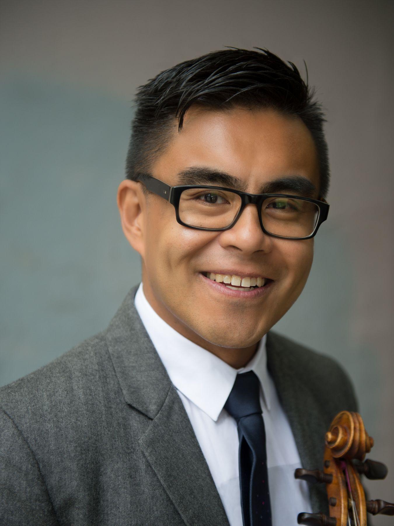 Doña wears a suit and glasses and smiles.