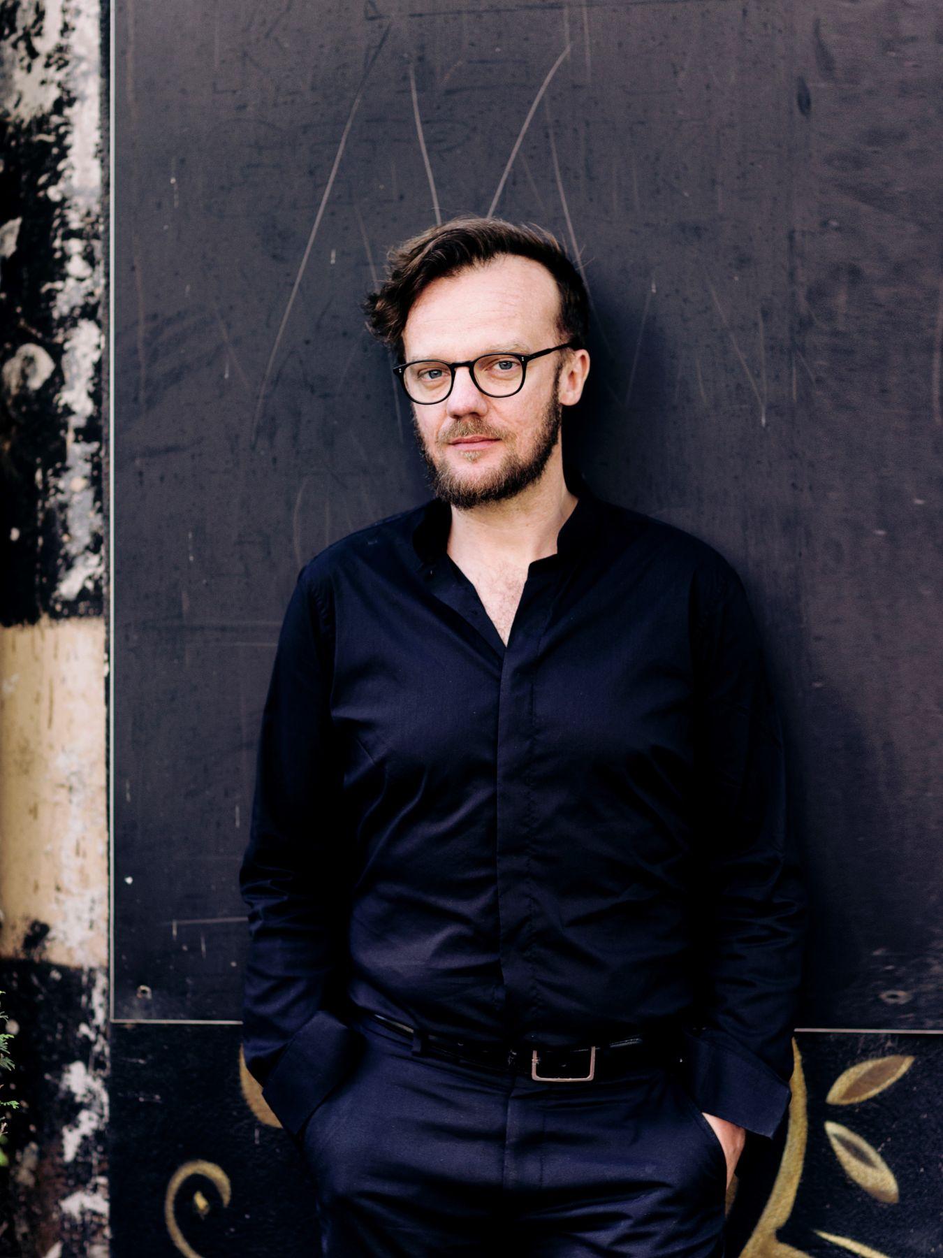 Oscar Bianchi wears dark clothing and leans casually against a wall.